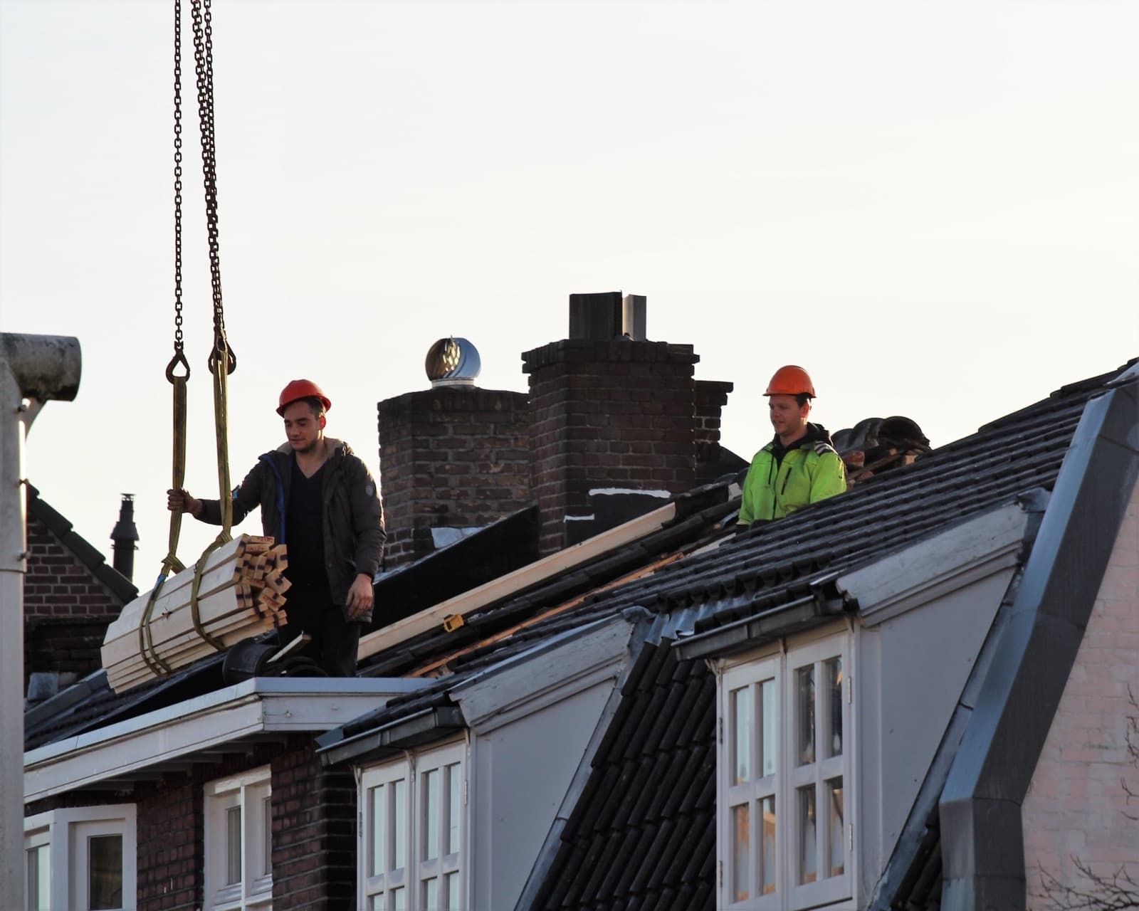 Dakdekkers hijsen panlatten op het dak tijdens een dakrenovatie