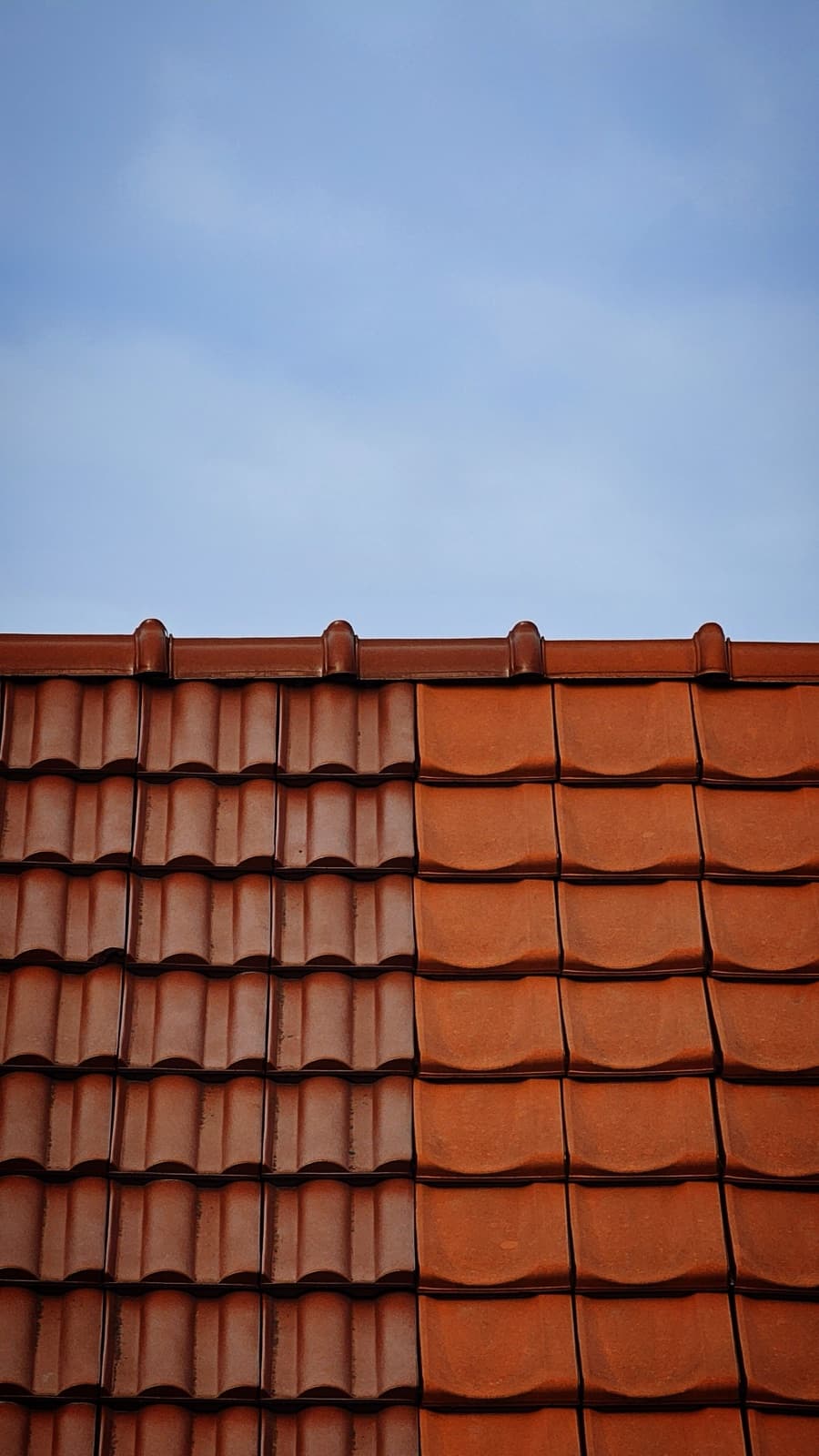 Nieuwe dakpannen naast verweerde oude pannen op een dak